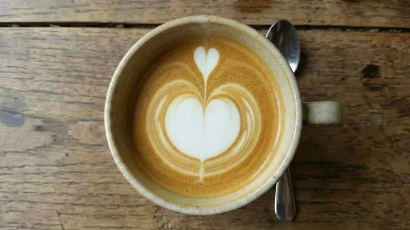 Overhead shot showing the final strike-through motion, pushing a thin stream of milk forward through the center to complete the pattern (this often leads to a heart shape for beginners)