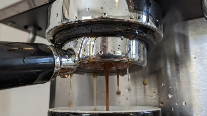 Close-up of an espresso machine group head leaking water and coffee from around the portafilter due to a failed gasket
