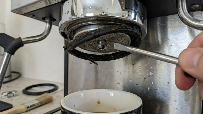 Prying the old, worn black rubber gasket out of the group head using a flathead screwdriver